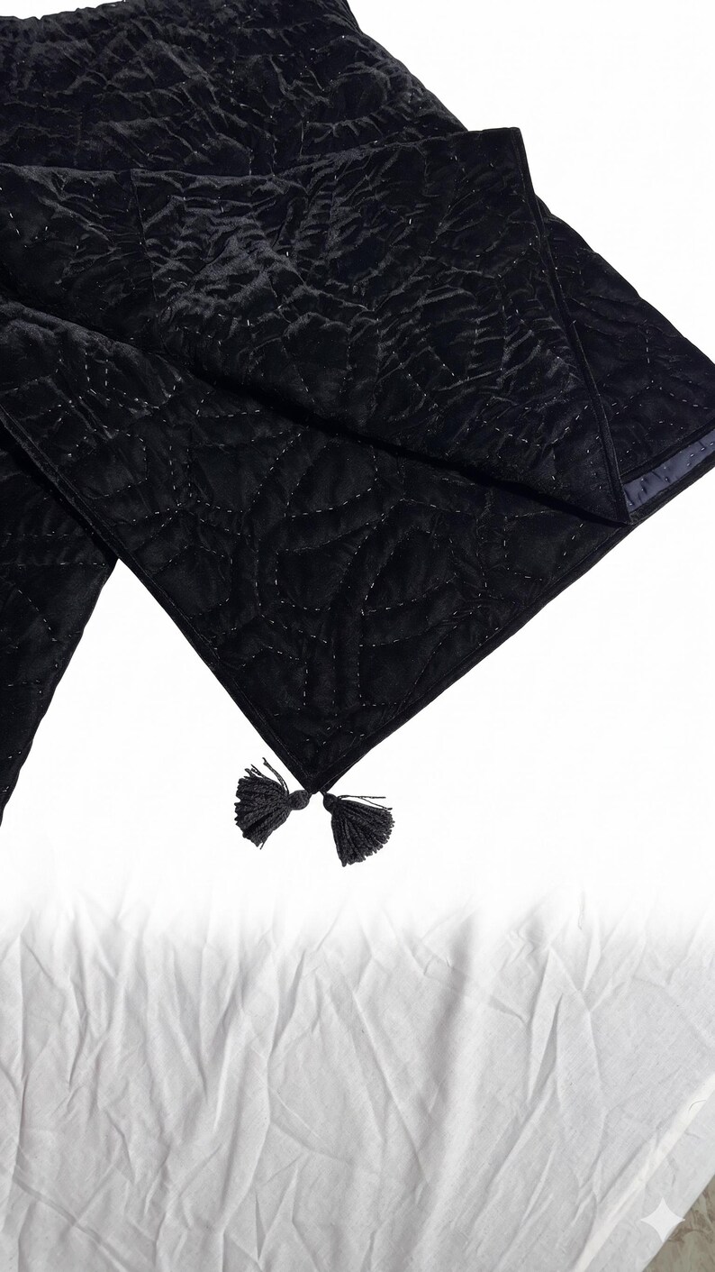 Puede incluir: Camino de mesa de terciopelo negro con un patr&oacute;n acolchado y borlas decorativas en los extremos. El camino de mesa est&aacute; hecho de una tela suave y texturizada.