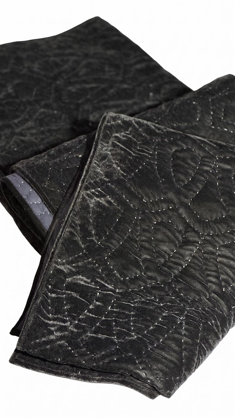 Puede incluir: Manta acolchada negra doblada con un patr&oacute;n de diamantes. La manta tiene una textura suave y aterciopelada y un borde gris oscuro. Las costuras son visibles, creando una superficie texturizada. La manta est&aacute; doblada sobre s&iacute; misma.