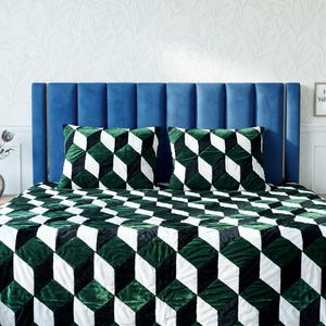 Peut inclure: Un lit avec une tête de lit en velours bleu, une couette à motifs géométriques et deux oreillers assortis. La couette et les oreillers présentent un motif répétitif de cubes verts, noirs et blancs. Une table de chevet en bois est visible sur le côté.