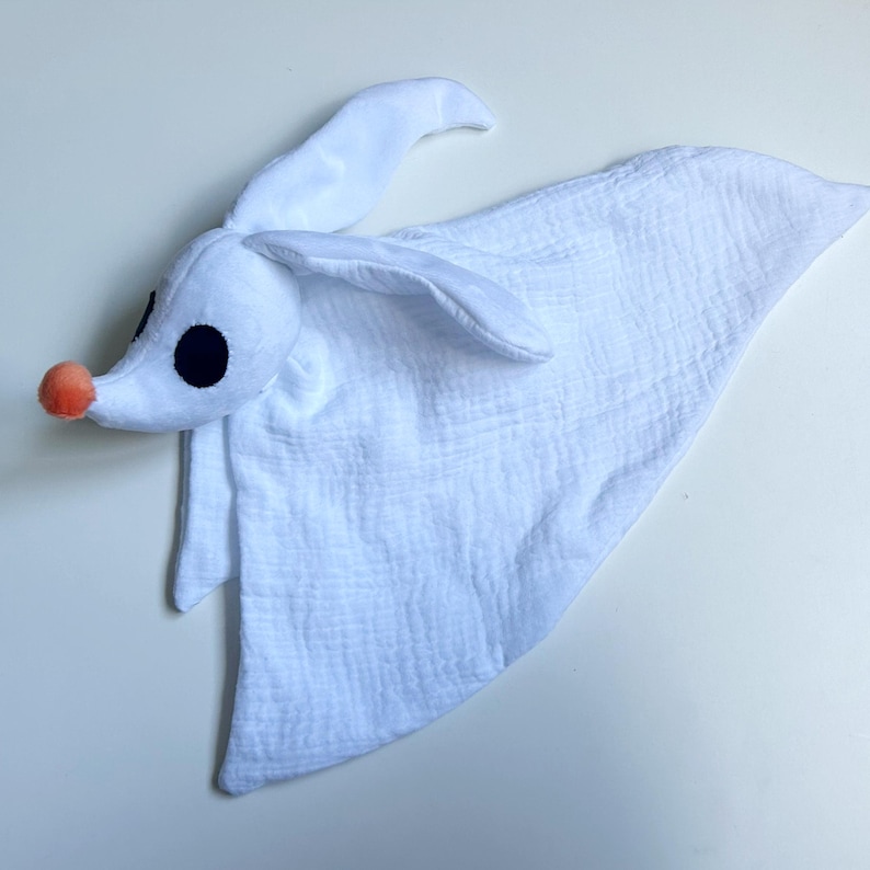 Op de afbeelding: Een wit pluche speeltje in de vorm van een spookhond met lange oren, een ronde oranje neus en grote zwarte ronde ogen. De kop zit vast aan een zacht, getextureerd wit stoffen lichaam dat als een deken naar beneden valt in een spookachtig silhouet.