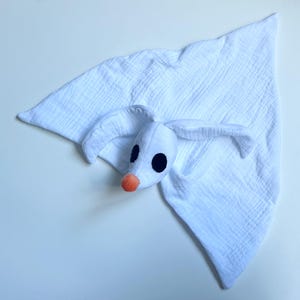 Op de afbeelding: Een wit mousseline knuffeldoekje met een pluche spookachtig karakterhoofd met lange slappe oren, grote zwarte ovale ogen en een kleine oranje neus. De stof heeft een gekreukelde textuur en is gevormd tot een zacht, driehoekig doekje.