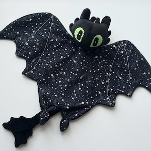 May include: A plush bat toy with a black body and wings. The wings are patterned with white stars on a dark background. The bat's head is black with green eyes.