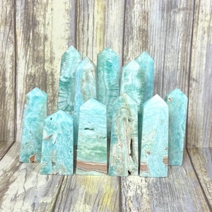 May include: A collection of turquoise-colored crystal towers with varying patterns and textures. The crystals are arranged on a wooden surface, showcasing their natural beauty and unique formations. The towers have a polished finish.