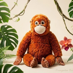 Puede incluir: Un muñeco de peluche de orangután con pelaje marrón, hocico blanco y ojos grandes y expresivos. El peluche está rodeado de follaje tropical, incluyendo hojas verdes grandes y enredaderas. La muñeca está sentada sobre una superficie clara.