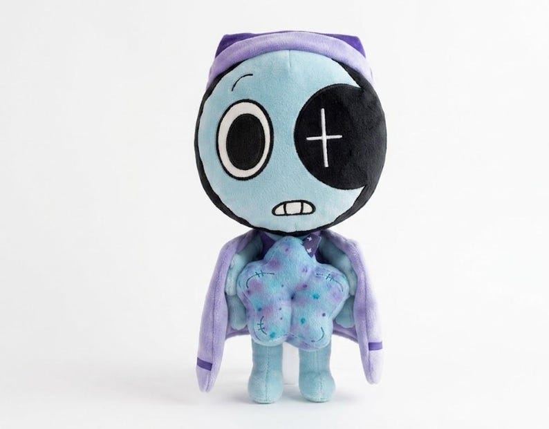 Pode incluir: Uma boneca de pel&uacute;cia com um rosto azul claro, um olho grande e um tapa-olho preto sobre o outro olho. Ela usa um chap&eacute;u e capa roxos e segura um objeto azul em forma de estrela. A boneca tem uma boca costurada e pernas azuis pequenas.