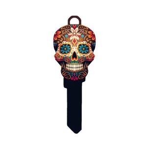 May include: A decorative key featuring a colorful sugar skull design. The skull is adorned with floral patterns in shades of orange, blue, and yellow against a dark brown background. The key's handle is brown, and the key's blade is black.