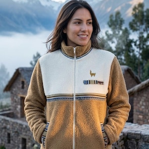 May include: A tan and cream-coloured fleece jacket with a high collar and a full-length front zip. The jacket features a small embroidered llama icon on the chest, decorative patterned trim across the chest and pockets, and long sleeves.