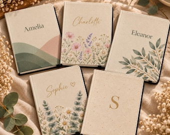 May include: Five rectangular notebooks with cream-colored covers. One features green and pink hills with the name Amelia. Another shows wildflowers and the name Charlotte. A third displays green leaves and the name Eleanor. A fourth has daisies, eucalyptus, and the name Sophie with a heart. The fifth features a gold letter S.