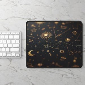 May include: Black rectangular mousepad featuring a celestial design with gold-colored suns, moons, stars, and constellations. The mousepad has a black border and is next to a white keyboard.