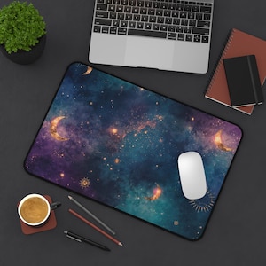 Könnte beinhalten: Rechteckige Schreibtischunterlage mit einem Himmelsdesign in Dunkelblau, Lila und Gold. Die Unterlage hat ein galaxieartiges Muster mit Monden, Sternen und Sonnen. Eine weiße Computermaus liegt auf der Unterlage.