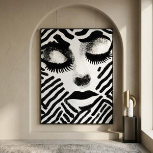 Peut inclure: Impression d'art abstrait en noir et blanc représentant un visage de femme aux yeux fermés et aux lèvres pleines. Le visage est entouré d'un motif zébré. L'œuvre est encadrée dans un cadre noir et accrochée à un mur beige.