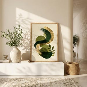 Peut inclure: Une impression d'art abstrait encadrée avec un fond beige, des coups de pinceau et des formes verts et dorés. L'œuvre est encadrée dans un cadre en bois clair. L'impression fait partie d'une collection de décoration intérieure.