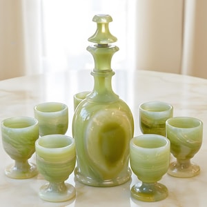 Könnte beinhalten: Ein grünes Onyx-Likör-Set, bestehend aus einer Karaffe mit Verschluss und sechs passenden kleinen Stielgläsern. Das Glas hat ein marmoriertes Aussehen mit Grün- und Weißtönen. Das Set steht auf einer marmorähnlichen Oberfläche.