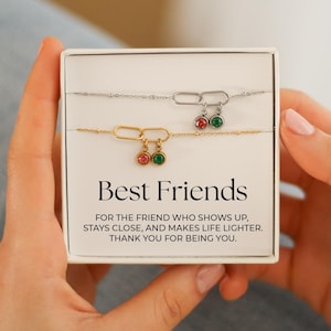 May include: A gift box containing two friendship bracelets. One bracelet is gold-toned, the other silver-toned. Each bracelet has a charm with red and green gemstones. The box reads "Best Friends".