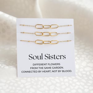 May include: Three gold-colored chain link bracelets displayed on a white card. The card reads "Soul Sisters" with the text "Different flowers from the same garden. Connected by heart, not by blood."