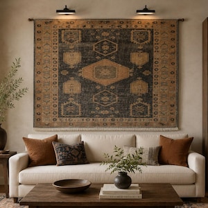 May include: A living room scene featuring a large, patterned rug hanging on the wall above a white sofa. Brown and rust-colored throw pillows and a wooden coffee table with a decorative bowl complete the cozy setting. A wooden bookshelf is on the right.