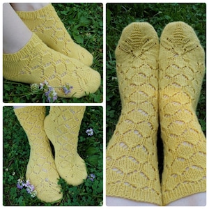 May include: A pair of yellow knitted socks with a lacy pattern. The socks are shown on a model's feet and on a grassy surface.