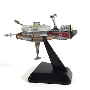 Puede incluir: Modelo detallado de Thunderbird 5, una estación espacial de la serie de televisión clásica. El modelo es plateado, marrón y rojo, montado sobre un soporte negro. El texto "Thunderbird 5" es visible.