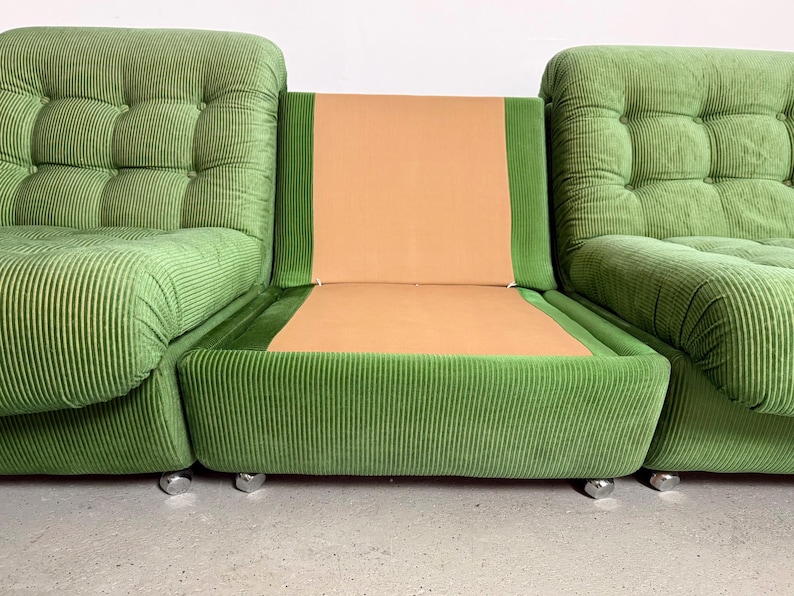 May include: A modular green corduroy sofa with a central tan seat and back. The sofa is composed of three sections, with the outer two featuring tufted cushions and the center section having a flat seat and back. The sofa sits on small, silver-colored feet.