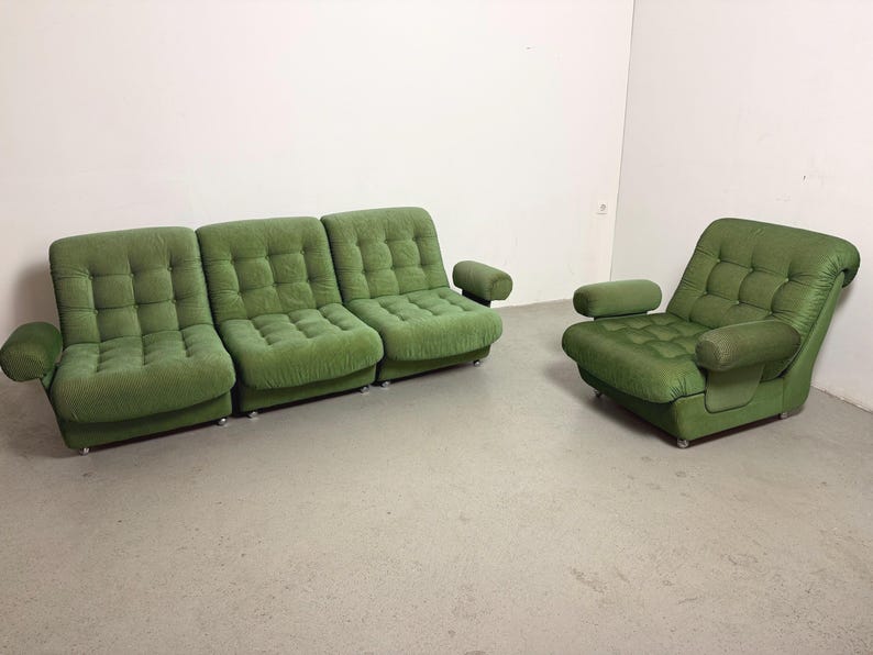 May include: A green upholstered sofa with three sections and a matching armchair. Both pieces have a tufted design and rounded armrests. The furniture is set against a white wall and a light gray floor.