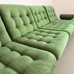 May include: A large, modular green corduroy sofa with a tufted design. The sofa has multiple sections, including a chaise lounge with an attached armrest. The fabric has a ribbed texture, and the cushions are button-tufted.