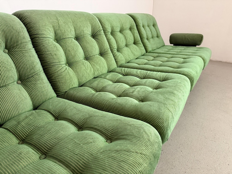 May include: A large, modular green corduroy sofa with a tufted design. The sofa has multiple sections, including a chaise lounge with an attached armrest. The fabric has a ribbed texture, and the cushions are button-tufted.