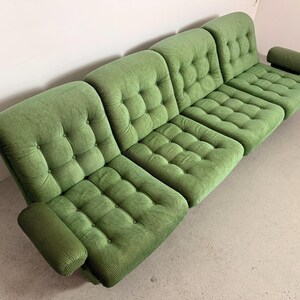 May include: A modular green corduroy sofa with a tufted design. The sofa is composed of several sections, including armrests and a headrest. The sections are arranged to create a comfortable seating arrangement. The sofa is a vibrant shade of green.