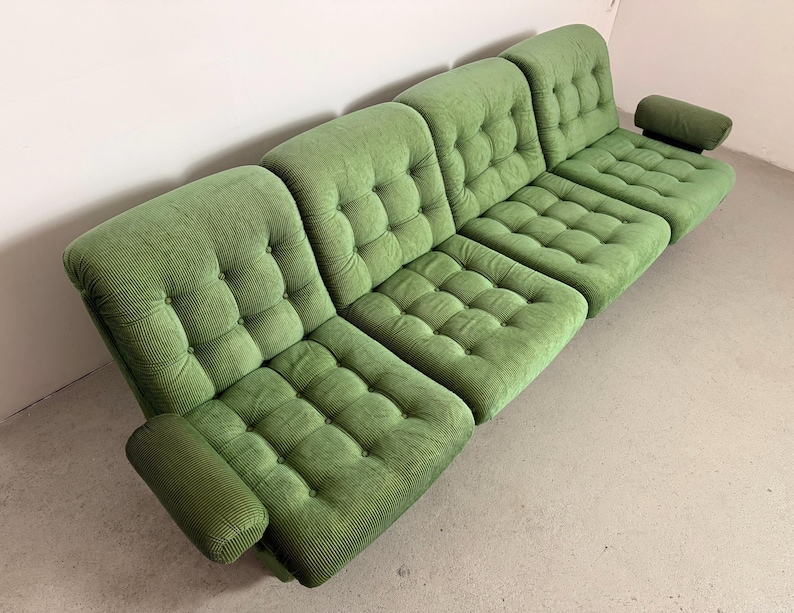 May include: A modular green corduroy sofa with a tufted design. The sofa is composed of several sections, including armrests and a headrest. The sections are arranged to create a comfortable seating arrangement. The sofa is a vibrant shade of green.