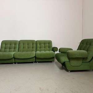 May include: A green, mid-century modern sofa and armchair set. The sofa has three sections with tufted cushions and rounded armrests. The armchair has a high back and matching armrests. Both pieces sit on low, silver legs.