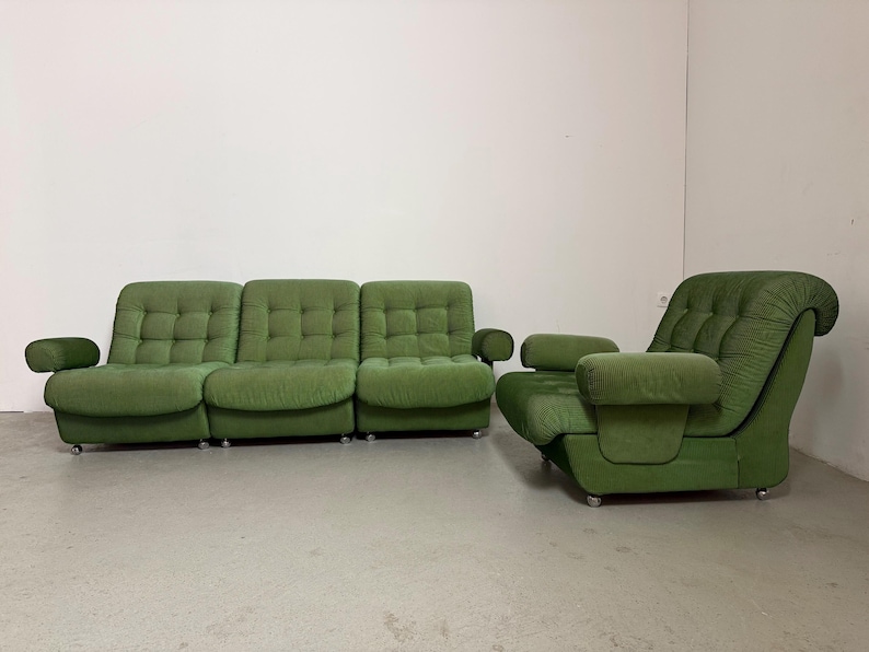 May include: A green, mid-century modern sofa and armchair set. The sofa has three sections with tufted cushions and rounded armrests. The armchair has a high back and matching armrests. Both pieces sit on low, silver legs.