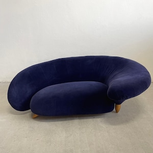 May include: A navy blue, curved sofa with a rounded back and seat. The sofa has a low profile and is supported by short, wooden legs. The upholstery appears to be a soft, velvet-like fabric.
