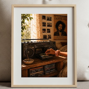 Può includere: Una fotografia incorniciata con un boombox vintage, un poster di Lauryn Hill e una collezione di CD. L'immagine è ambientata in una stanza con luce naturale, creando un'atmosfera nostalgica e artistica. Si vede una mano interagire con il boombox.