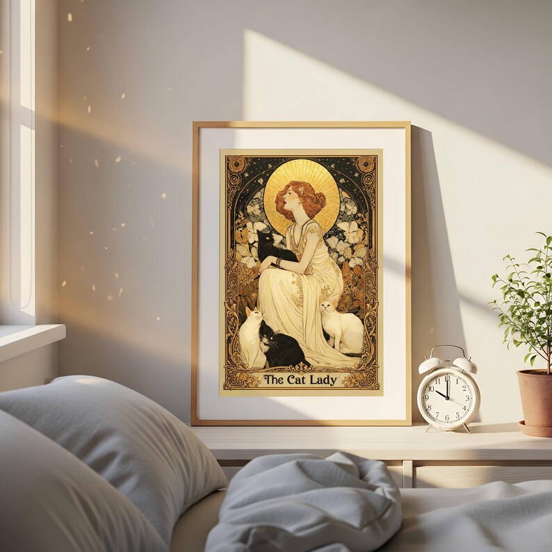 May include: A framed art print featuring a woman in a flowing gown surrounded by cats. The artwork has a vintage style with gold and cream tones. The text "The Cat Lady" is at the bottom of the print.
