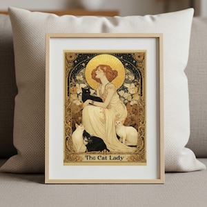 May include: A framed art print titled The Cat Lady featuring an illustration of a person in a long cream dress with a golden halo, surrounded by two black cats and two white cats, set within an ornate gold and black decorative border.