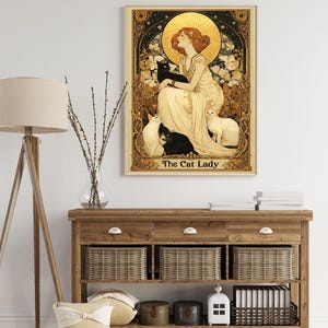 May include: A rectangular wall art print titled The Cat Lady, featuring a woman in a flowing cream dress surrounded by black and white cats, set against a gold halo and ornate black and gold floral border with intricate decorative details.