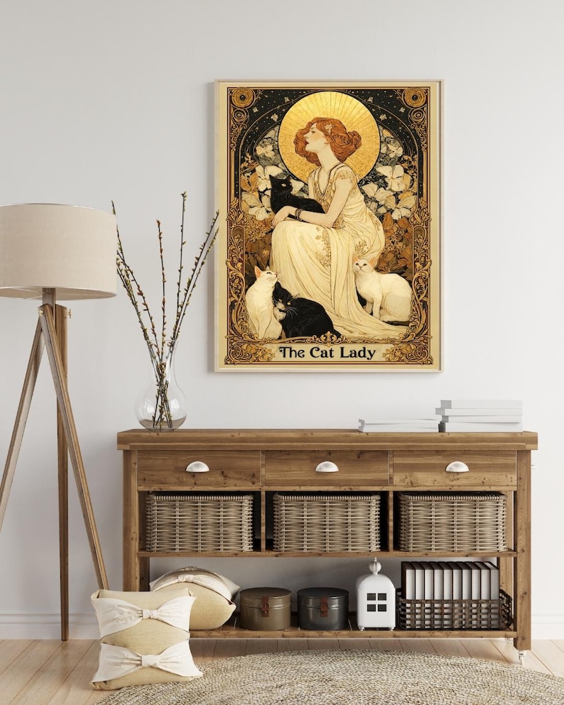 May include: A rectangular wall art print titled The Cat Lady, featuring a woman in a flowing cream dress surrounded by black and white cats, set against a gold halo and ornate black and gold floral border with intricate decorative details.