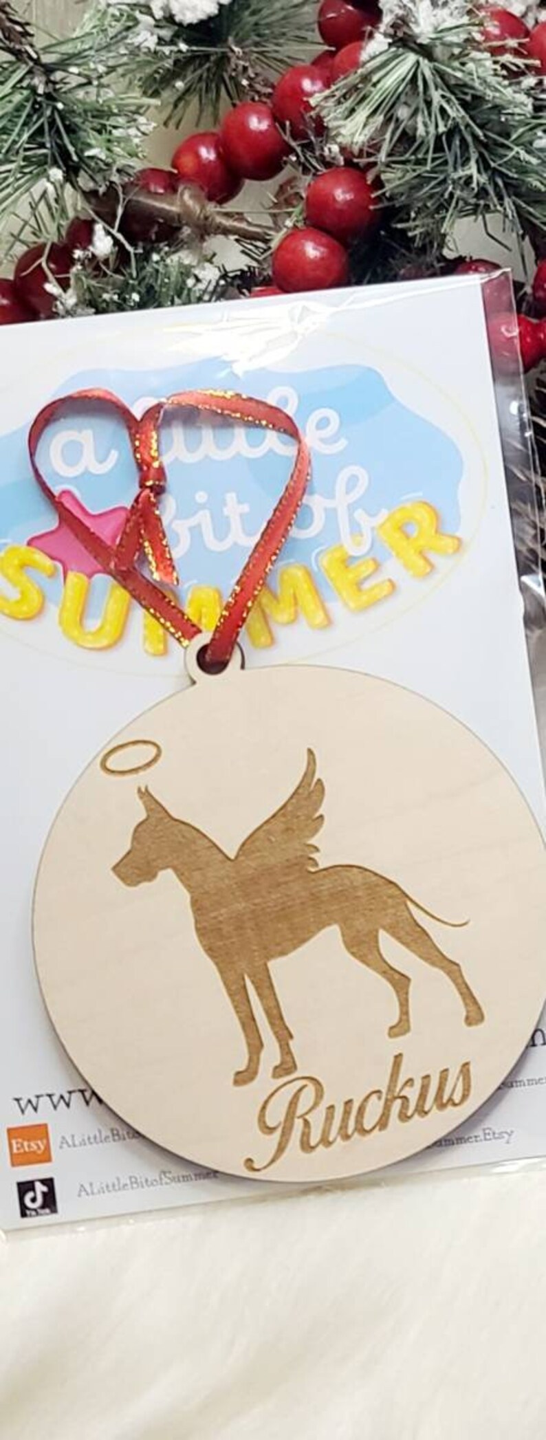 K&ouml;nnte beinhalten: Ein Holz-Anh&auml;nger mit einer Silhouette eines Hundes mit Fl&uuml;geln und einem Heiligenschein. Der Hund ist ein Deutscher Dogge. Der Anh&auml;nger ist mit dem Namen "Ruckus" graviert.