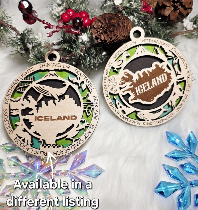 May include: Two circular wooden ornaments featuring a cutout map of Iceland with the text ICELAND in the center. The outer rings are engraved with locations like Thingvellir, Skaftafell, and Reykjavik, layered over a green and blue background.