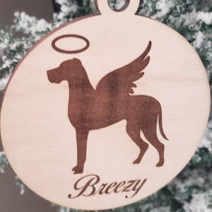 K&ouml;nnte beinhalten: Ein Holz-Anh&auml;nger mit einer Silhouette eines Hundes mit Fl&uuml;geln und einem Heiligenschein. Der Anh&auml;nger ist mit dem Namen "Breezy" graviert.