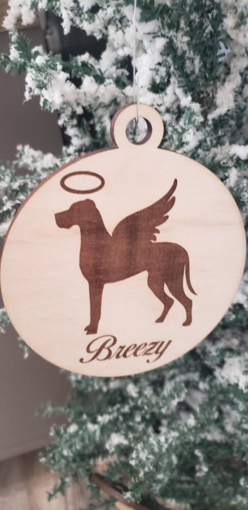 K&ouml;nnte beinhalten: Ein Holz-Anh&auml;nger mit einer Silhouette eines Hundes mit Fl&uuml;geln und einem Heiligenschein. Der Anh&auml;nger ist mit dem Namen "Breezy" graviert.