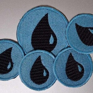 May include: A collection of five circular embroidered patches in light blue, each featuring a centered black water droplet icon with a small white highlight. The patches vary in size and are arranged in a cluster, showcasing detailed stitching.