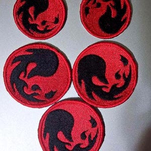 May include: Five circular embroidered patches featuring a black flame-like design centered on a vibrant red background. The patches are arranged in a cluster, with two smaller patches at the top and three larger patches positioned below them.