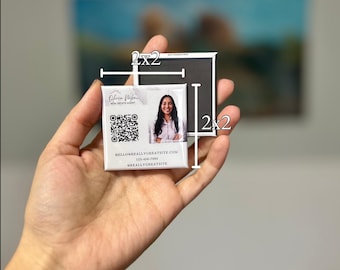 May include: A 2x2 inch square magnet featuring a real estate agent's photo, a QR code, and contact information. A second 2x2 inch black magnet is also shown. The text on the magnet reads: "Hello@reallygreatsite.com" and "123-456-7890".