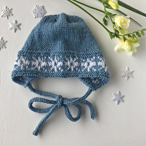 May include: A blue knitted baby hat with a white snowflake pattern around the brim. The hat has a tie that can be tied under the chin.