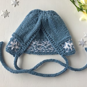 May include: A blue knitted baby hat with white snowflake designs and matching ties. The hat is folded down and the ties are tied together.