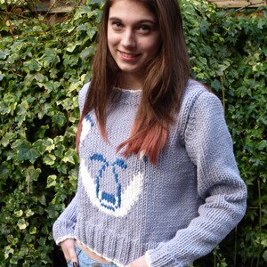May include: A light purple knitted jumper with a white and blue fox design. The jumper has a cropped length and a ribbed hem.