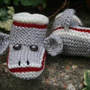 May include: A pair of gray knitted baby booties with red and white stripes, featuring a monkey face with black button eyes.