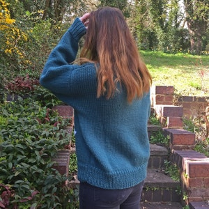 May include: A teal blue knitted sweater with a relaxed fit. The sweater is made of a soft, chunky yarn and has a simple, classic design.
