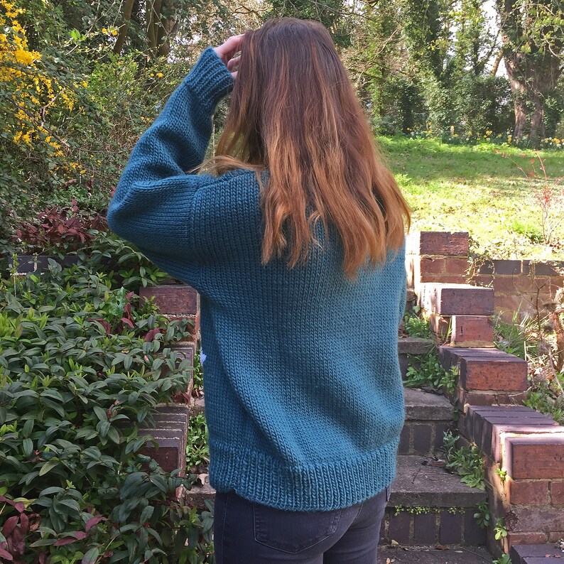 May include: A teal blue knitted sweater with a relaxed fit. The sweater is made of a soft, chunky yarn and has a simple, classic design.