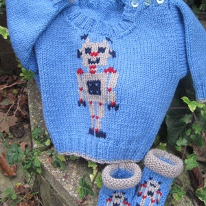 May include: A blue knitted sweater with a robot design and matching blue knitted booties. The robot is gray, white, red, and black.